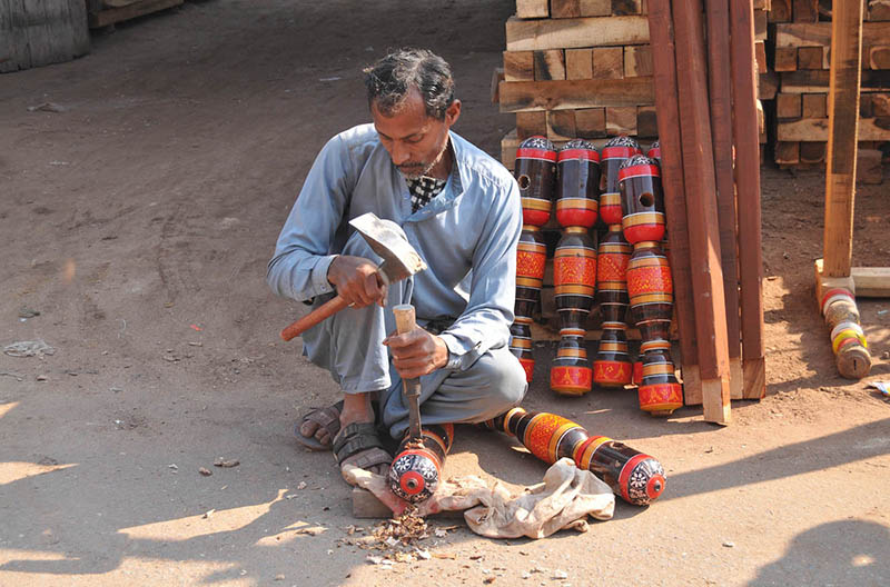 An artisan carefully carves part of traditional wooden bed craft by hand at his roadside workshop in the city