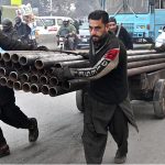 Labourers pulling and pushing handcart loaded with heavy Iron pipes to deliver in a local market