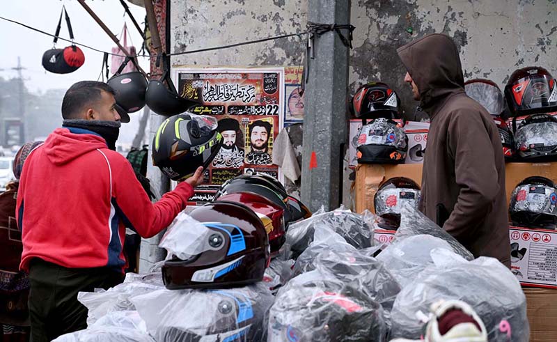 A motorcyclist purchases a helmet from a roadside vendor