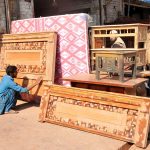 A worker is busy polishing and arranging wooden furniture displayed outside a local workshop to attract customers in the city